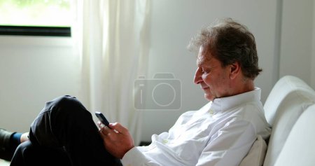 Foto de Senior man working from home holding smartphone checking emails - Imagen libre de derechos