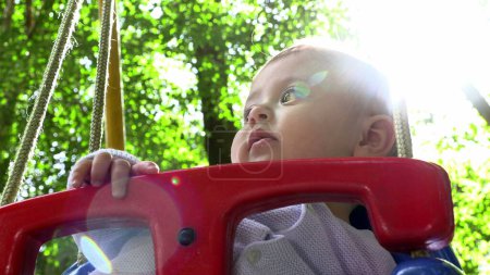 Foto de Bebé sentado en el columpio del parque infantil observando con la luz del sol del lente-destello - Imagen libre de derechos