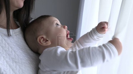 Téléchargez les photos : Bébé jouant avec fenêtre rideau à la maison bébé tenant rideau de soie - en image libre de droit