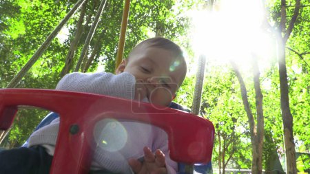 Téléchargez les photos : Bébé garçon mignon à l'extérieur avec aire de jeux swing parc avec éclat artistique soleil - en image libre de droit