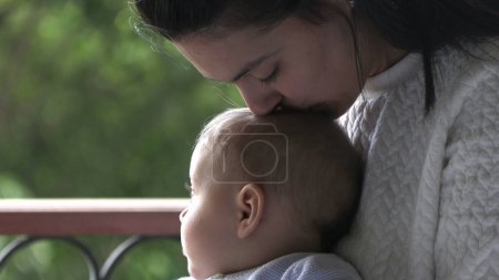 Foto de Candid madre besos bebé infante hijo casual auténtico momento por ventana - Imagen libre de derechos