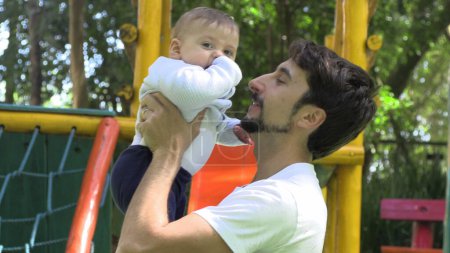 Foto de Papá sosteniendo bebé hijo en parque infantil al aire libre amante relación auténtica - Imagen libre de derechos