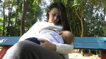 Téléchargez les photos : Casual authentique mère tenant bébé dans le parc en dehors de l'allaitement - en image libre de droit