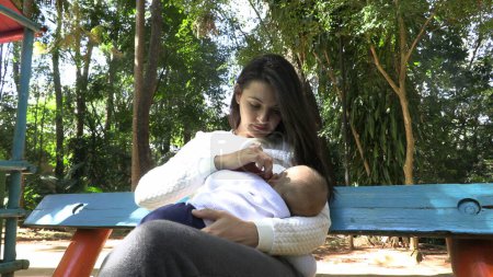 Foto de Casual auténtica madre sosteniendo al bebé en el parque fuera de la lactancia materna - Imagen libre de derechos