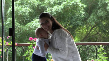 Téléchargez les photos : Authentique mère et bébé enfant ensemble par la fenêtre souriante et heureuse - en image libre de droit
