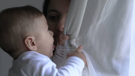 Téléchargez les photos : Mère tenant bébé jouant avec la fenêtre rideau - en image libre de droit