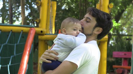 Téléchargez les photos : Papa tenant bébé fils au parc extérieur aire de jeux aimer relation authentique - en image libre de droit