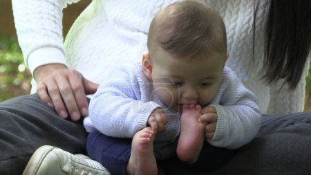 Téléchargez les photos : Mère et bébé au parc bébé mettre le pied dans la bouche - en image libre de droit