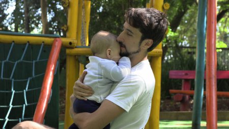 Téléchargez les photos : Père tenant bébé fils à l'extérieur au parc de l'aire de jeux embrasser et aimer - en image libre de droit