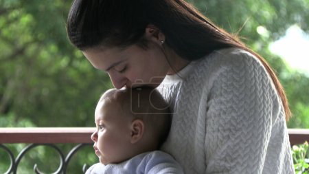 Téléchargez les photos : Maman embrasser bébé bébé fils à côté de la fenêtre - en image libre de droit