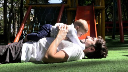 Téléchargez les photos : Père soulevant bébé fils dans les airs au parc père occasionnel soulevant bébé vers le haut dans les airs au terrain de jeux - en image libre de droit