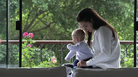 Téléchargez les photos : Mère tenant bébé fils à côté de la fenêtre donnant sur la vue - en image libre de droit