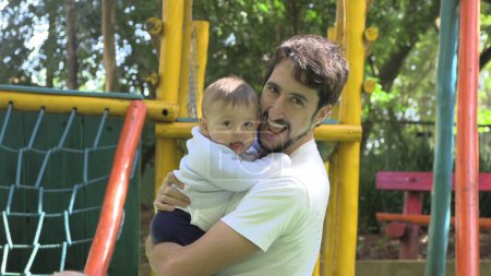 Téléchargez les photos : Père tenant bébé fils regardant à la caméra authentique sourire occasionnel et relation - en image libre de droit