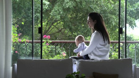 Foto de Mamá sosteniendo bebé hijo niño con vistas a la vista mirando por la ventana - Imagen libre de derechos