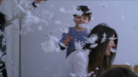 Mother and children admist feather plumage in the air being thrown everywhere capturing carefree blissful family moment in super slow motion at 1000 fps, authentic laughter and smiles