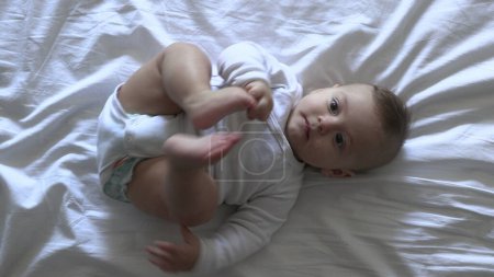 Téléchargez les photos : Adorable bébé mignon dans le lit tenant pied - en image libre de droit
