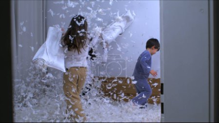 Photo for Happy moment of children and mom having a pillow fight with feathers flying everywhere in the air in slow motion 1000 fps, siblings standing in bed engaged in play - Royalty Free Image