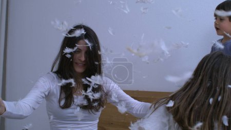 Mother and children throwing feathers in the air in super slow motion at 1000 fps. Woman bonding with kids in post pillow battle as plumage falls everywhere