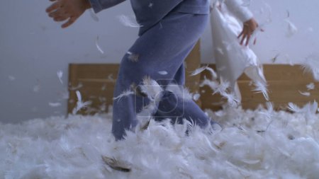 Photo for Children playing pillow fight standing in bed in ultra slow motion 1000 fps with feathers flying everywhere capturing authentic childhood happiness - Royalty Free Image