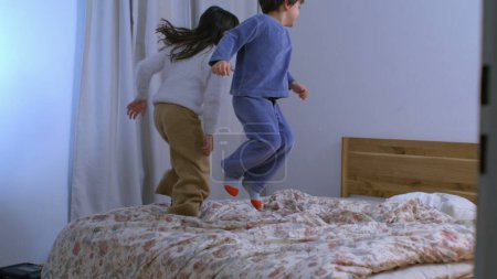 Téléchargez les photos : Bonne petite fille rebondissant au lit au ralenti, frères et sœurs sautant en pyjama - en image libre de droit