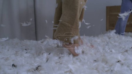 Photo for Child bouncing up and down in bed in slow motion with many feathers flying in the air in the midst of pillow fight, kids jumping up and down - Royalty Free Image