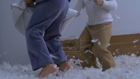 Children bouncing in bed in the midst of pillow battle with feathers flying in the air captured with a high speed camera