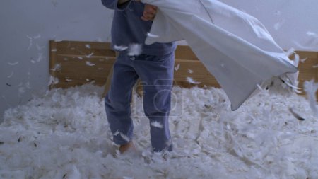 Photo for Siblings engaged in pillow fight jumping up and down on bed while feathers fly everywhere in the air - Royalty Free Image