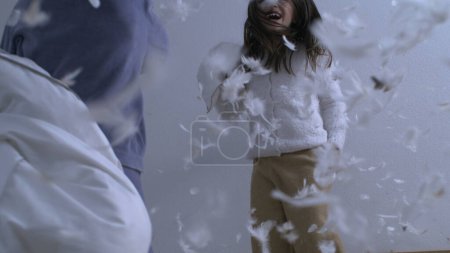 Photo for Siblings having pillow fight while bouncing in bed captured in super slow motion at 1000 fps with feathers flying mid-air everywhere, happy carefree childhood emotion - Royalty Free Image
