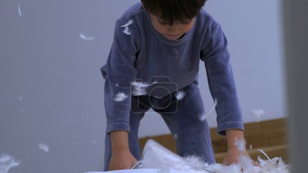 Feathers falling everywhere while little boy picks up unzipped pillow standing in bed wearing pajamas, child covered in plumage fly in air-SD 480p