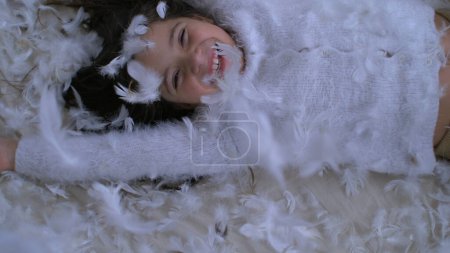 Happy Little Girl Tombant sur le lit avec des milliers de plumes volantes dans les airs, capturées avec une caméra haute vitesse à 1000 ips. Enfant souriant au milieu du plumage