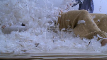Little girl falling in plumage surface with feathers flying in the air in super slow motion captured at 1000 fps. Carefree child having fun amidst feather bed