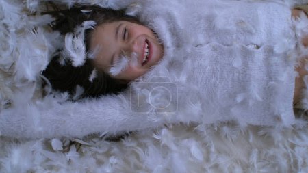 Happy Little Girl Falling on bed with thousands of feathers flying in the air, captured with a High-Speed Camera at 1000 fps. Child smiling amidst plumage