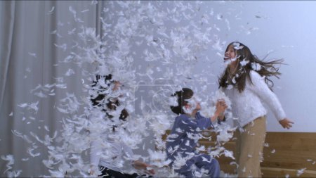 Photo for Carefree moment of family having fun with thousands of feathers bouncing in bed in super slow motion at 1000 fps, woman throws plumage into children, authentic happy memory - Royalty Free Image