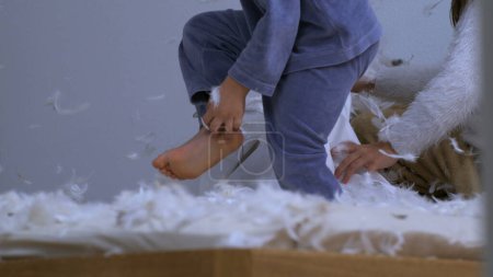 Photo for Bed covered with feathers with children in background doing a mess during pillow fight battle, plumage flies in the air in slow motion - messy bedroom - Royalty Free Image