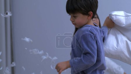 Photo for Little boy defending himself with pillow from sister amidst in pillow battle captured in slow motion - Royalty Free Image