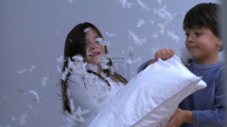 Téléchargez les photos : Petit frère et sœur se battent avec des plumes volantes partout capturées au ralenti à 1000 ips. Enfants dans une authentique mémoire heureuse - en image libre de droit