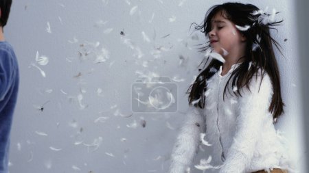 Photo for Little girl unzipping pillow and shaking feathers making them fly in the air everywhere in super slow motion at 1000 fps. Child making a mess in bedroom after pillow battle - Royalty Free Image