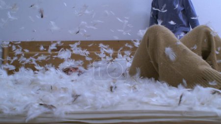 Foto de Niña cayendo en la superficie del plumaje con plumas volando en el aire en cámara súper lenta capturada a 1000 fps. Niño despreocupado divirtiéndose en medio de la cama de plumas - Imagen libre de derechos