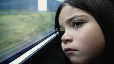 Foto de Triste niña de un año con mirada contemplativa, apoyada en la ventana del tren durante el viaje mirando fijamente pasar con emoción deprimida pensativa - Imagen libre de derechos