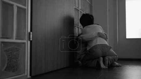 Photo for Small brother embraces sad depressed sister seated in moody dark corridor covering face, compassionate hug during hard times, family love and unity in black and white - Royalty Free Image