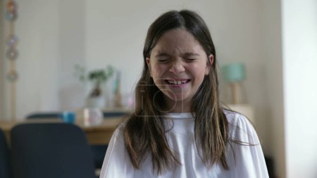 Joyful 8-Year-Old Girl Laughing at Camera, Close-Up Face in Living Room. Happy person, child's real life laugh and smile