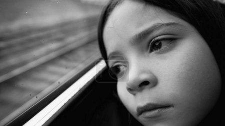 Foto de Triste niño deprimido mirando la vista desde la ventana del tren desde el asiento del pasajero. Primer plano niña sintiendo miedo y melancolía en blanco y negro, monocromo - Imagen libre de derechos