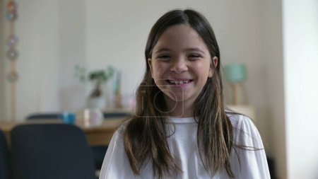 Foto de Alegre niña de 8 años riéndose de la cámara, de cerca la cara en la sala de estar. Persona feliz, la vida real del niño risa y sonrisa - Imagen libre de derechos