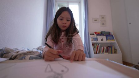Téléchargez les photos : Enfant concentré s'adonnant à des activités de dessin à la maison, à la plume et à l'artisanat du papier dans la chambre - en image libre de droit