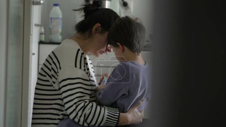 Téléchargez les photos : Mère attentionnée consolant petit fils pleurant dans la cuisine franche scène. Maman embrassant enfant blessé, franc et tendre - en image libre de droit