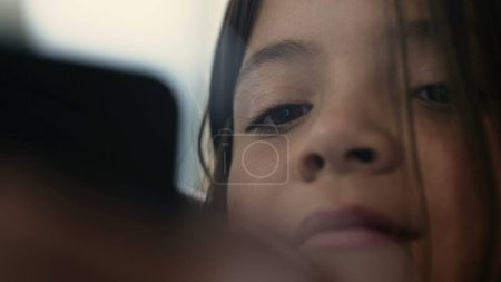 Großaufnahme Gesicht und Augen eines kleinen Mädchens starren auf Smartphone-Gerät scrollen Online-Medien. Kind hypnotisiert von Unterhaltungsinhalten