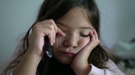 Foto de Niña cansada frotando el ojo con el dedo, cansada niña cansada sintiendo fatiga tarde en la noche cara de cerca - Imagen libre de derechos