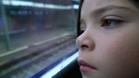 Foto de Cara de primer plano del niño reflexivo apoyado en la ventana del tren mirando la llegada de la estación de la plataforma. Macro primer plano de contemplativa niña de 8 años que llega a destino - Imagen libre de derechos
