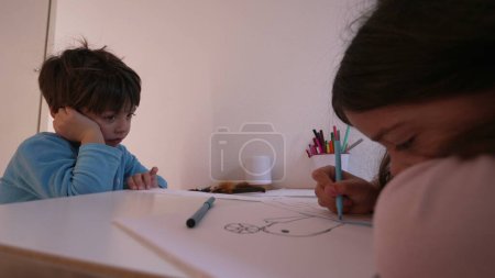 Photo for Upset Boy Feeling Bored While Sister Draws, Authentic Sibling Emotions. Child feeling withdrawn with hand holding head feeling boredom and sadness - Royalty Free Image