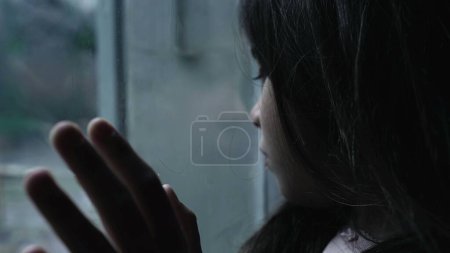 Foto de Enfermedad mental infantil representación de una niña pequeña luchando contra la depresión y la valía apoyada en una ventana de vidrio mirando fijamente a la vista en una escena de mal humor - Imagen libre de derechos